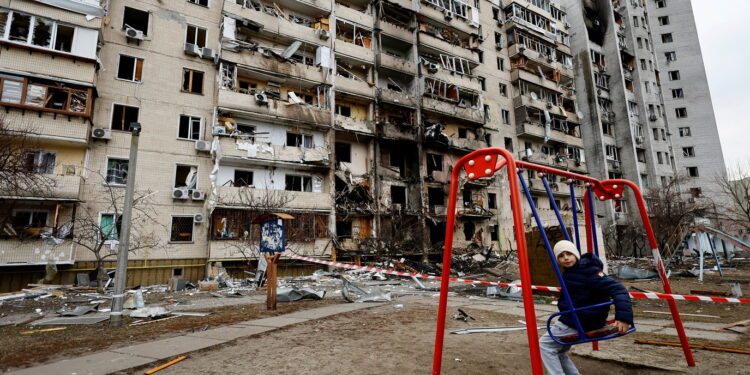 A child sits on a swing in front of a damaged residential building, after Russia launched a massive military operation against Ukraine, in Kyiv, Ukraine February 25, 2022. REUTERS/Umit Bektas     TPX IMAGES OF THE DAY